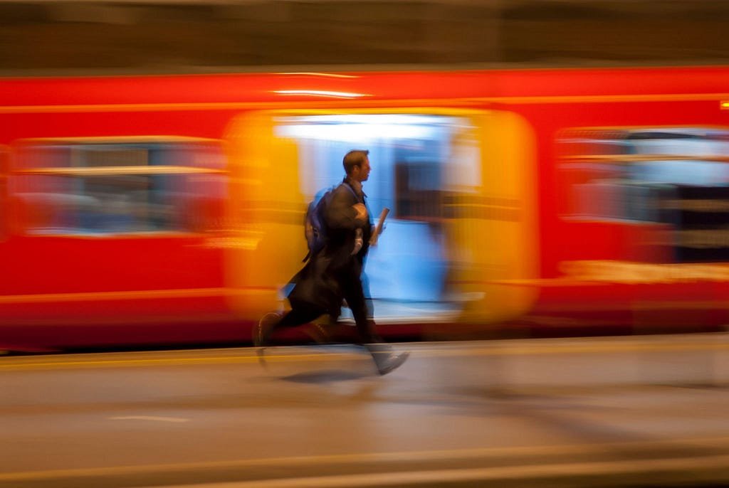 A man runs past a bright orange train to catch a train at Paddington station.