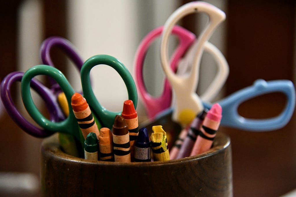 A wooden cup holds a pair of scissors and a colorful assortment of crayons.
